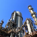 A towering industrial plant under a vivid blue sky, showcasing its intricate architecture and industrial prowess.